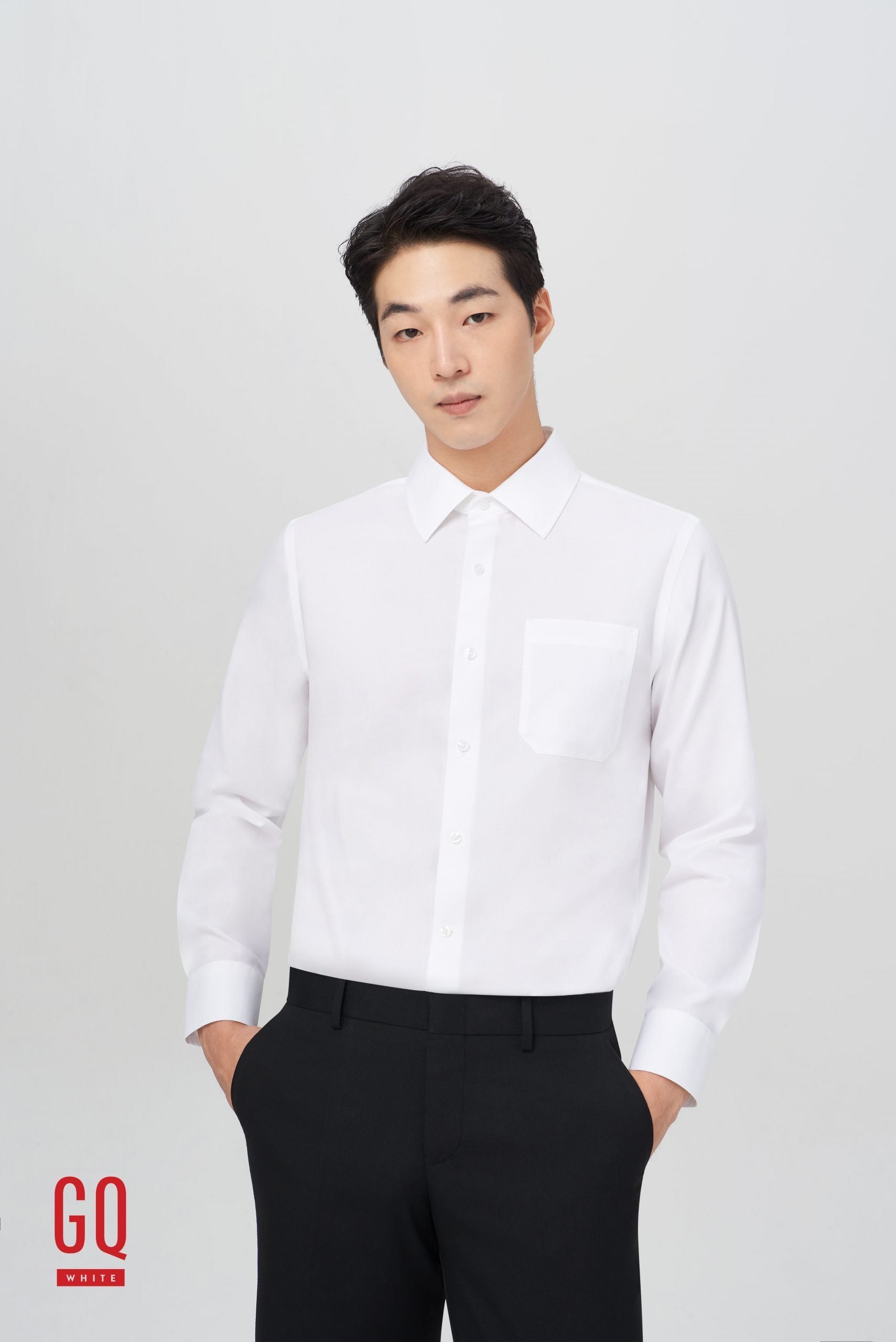 Man in GQWhite men's dress shirt and black pants stands with his hands in his pockets.